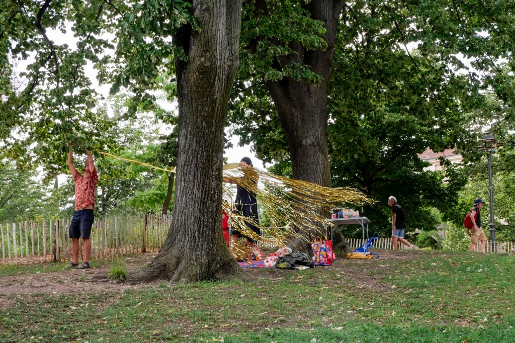 Photo couleur. Marseille, parc Longchamp : un couple installe une guirlande entre deux arbres.
