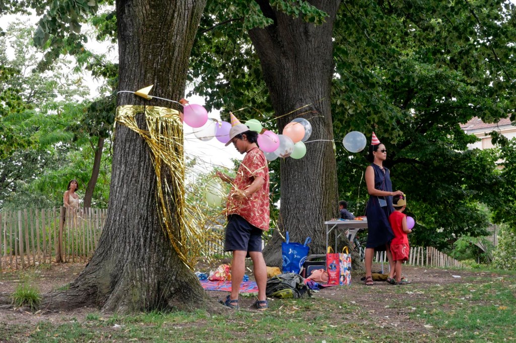 Photo couleur. Marseille, parc Longchamp : un couple attend les invités pour l'anniversaire de leur fils. Guirlande et ballons de baudruche sur un fil.