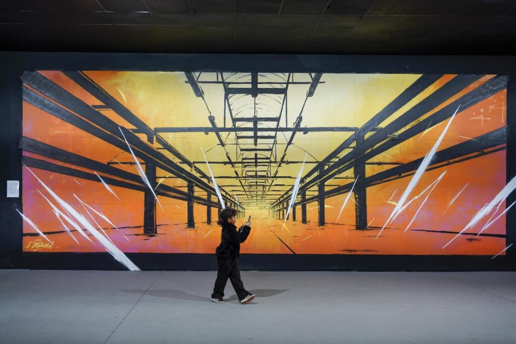 Marseille : street art. Un enfant avec un téléphone portable devant une oeuvre murale orange et jaune avec des lignes convergentes