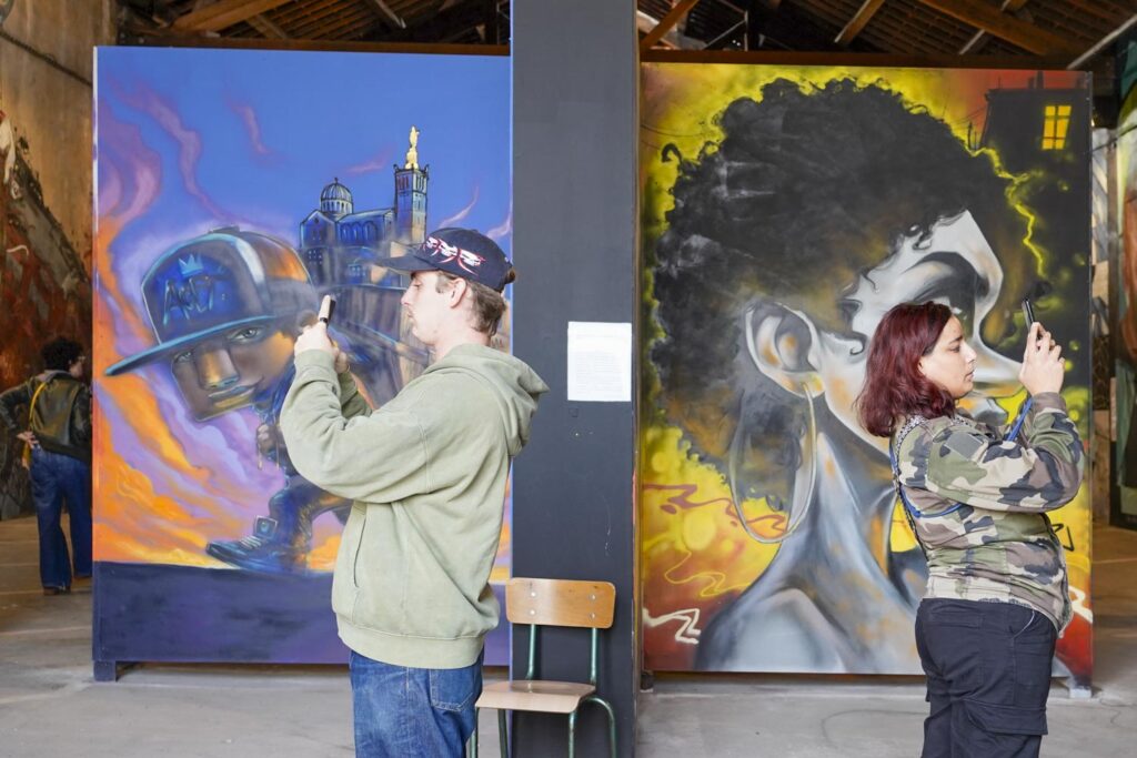 Marseille : street art. Un homme et une femme de profil, dos à dos photographient avec leurs portables devant deux portraits peints sur un mur.